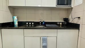 Eine kleine Küche mit weißen Schränken, einer schwarzen Arbeitsplatte, einer Mikrowelle und einem Spülbecken.