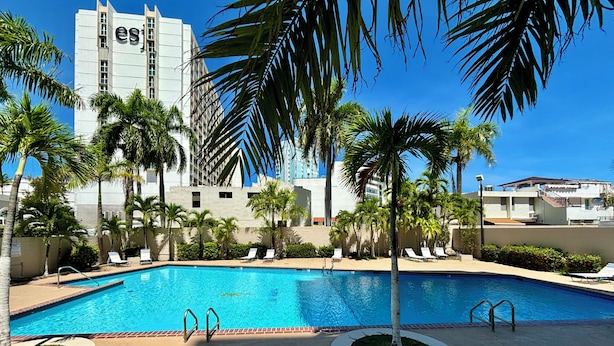 Ein Swimmingpool mit Liegestühlen und Palmen, umgeben von Gebäuden.