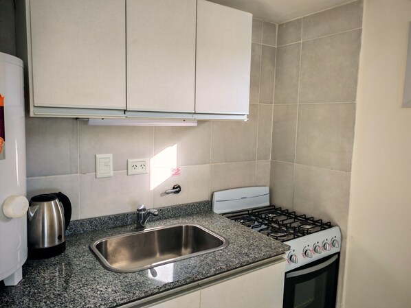 Una cocina compacta con un lavamanos de acero inoxidable, una estufa a gas y un hervidor.