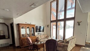 Ein geräumiges Wohnzimmer mit Holzdielen, einem großen Fenster, einem Holzschrank, einem Fernseher und einem Kamin.