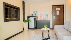 Un moderno vestíbulo de hotel con un sofá, una mesita con una planta, un refrigerador y una puerta de madera con un letrero de número.