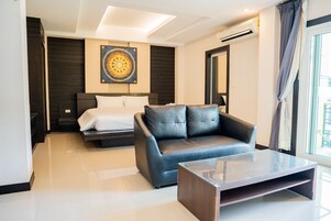 Quarto de hotel moderno com uma cama, um sofá de couro, uma mesa de centro de vidro e uma janela grande com cortinas.