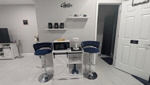 A kitchenette with a microwave, coffee maker, and tea and coffee containers. There are two bar stools and a small shelf with mugs. - Blue Dream Sunrise "Your Journey, Our Passion" Cozy retreat in lovely Lakeland (Lakeland)