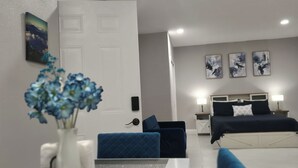 A modern bedroom with a bed, bedside tables, and a nightstand. There is a door with a painting above it and a vase with flowers on a table. - Blue Dream Sunrise "Your Journey, Our Passion" Cozy retreat in lovely Lakeland (Lakeland)