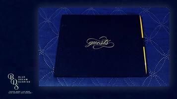 Ein dunkelblauer Ordner mit der goldenen, verschnörkelten Aufschrift "guests", platziert auf einem blauen Hintergrund mit dezentem geometrischen Muster.