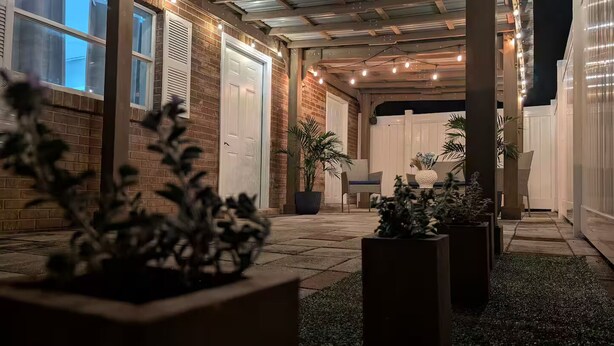 A covered outdoor patio area with brick walls, potted plants, and a white fence in the background. - Blue Dream Sunrise "Your Journey, Our Passion" Cozy retreat in lovely Lakeland (Lakeland)