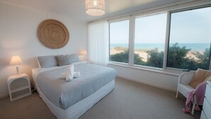 Quarto com uma cama grande, vista para a praia e um painel de parede redondo trançado.