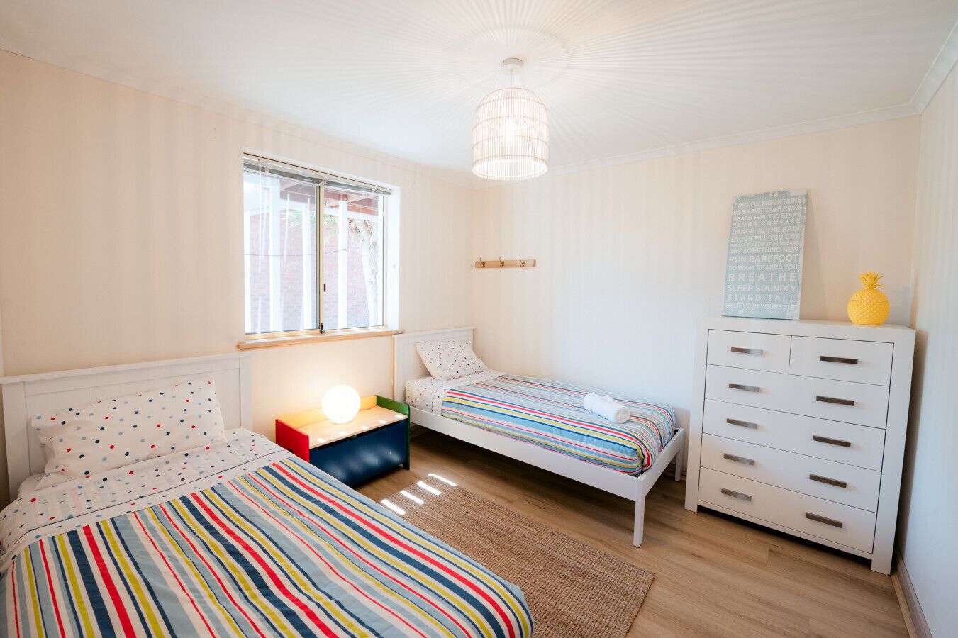 A bedroom with two beds, a dresser, a lamp, and a window.
