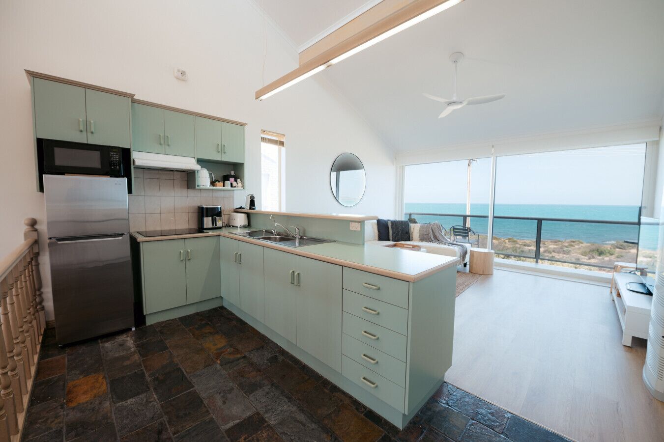 Una cucina moderna con frigorifero integrato, forno a microonde e macchina del caffè. Una grande finestra offre vista sull'oceano.