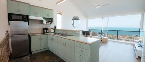 Una cucina moderna con frigorifero integrato, forno a microonde e macchina del caffè. Una grande finestra offre vista sull'oceano.