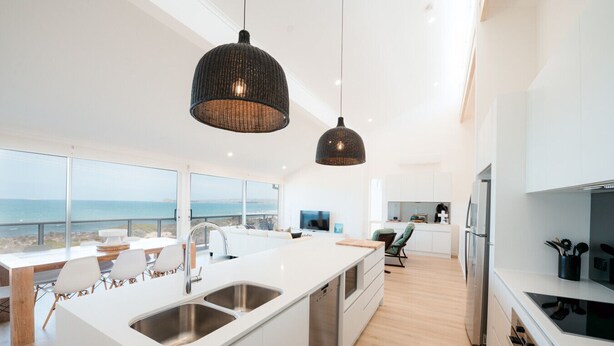 Cozinha moderna com uma ilha grande, armários brancos e vista para o mar.
