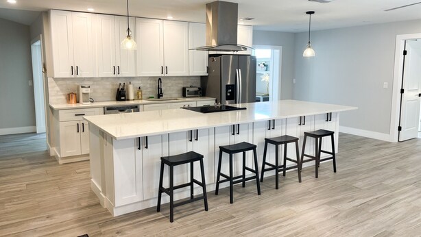 A modern kitchen with white cabinets, a large island with bar stools, stainless steel appliances, and pendant lighting. - 3 Bedroom Sunny Cape Coral Escape, 3 blocks from Lee Health, no cleaning fee! (Cape Coral)