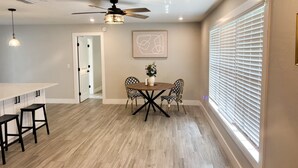 A dining area with a wooden table, four chairs, a ceiling fan, and a window with blinds. - 3 Bedroom Sunny Cape Coral Escape, 3 blocks from Lee Health, no cleaning fee! (Cape Coral)