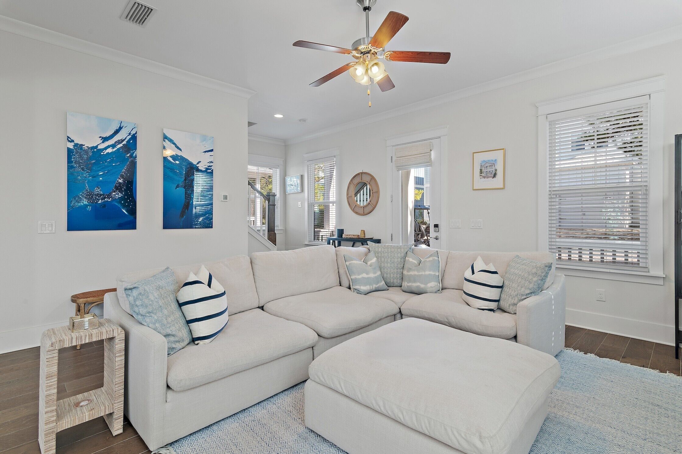 A modern living room with a sectional sofa, a ceiling fan, and artwork on the walls.