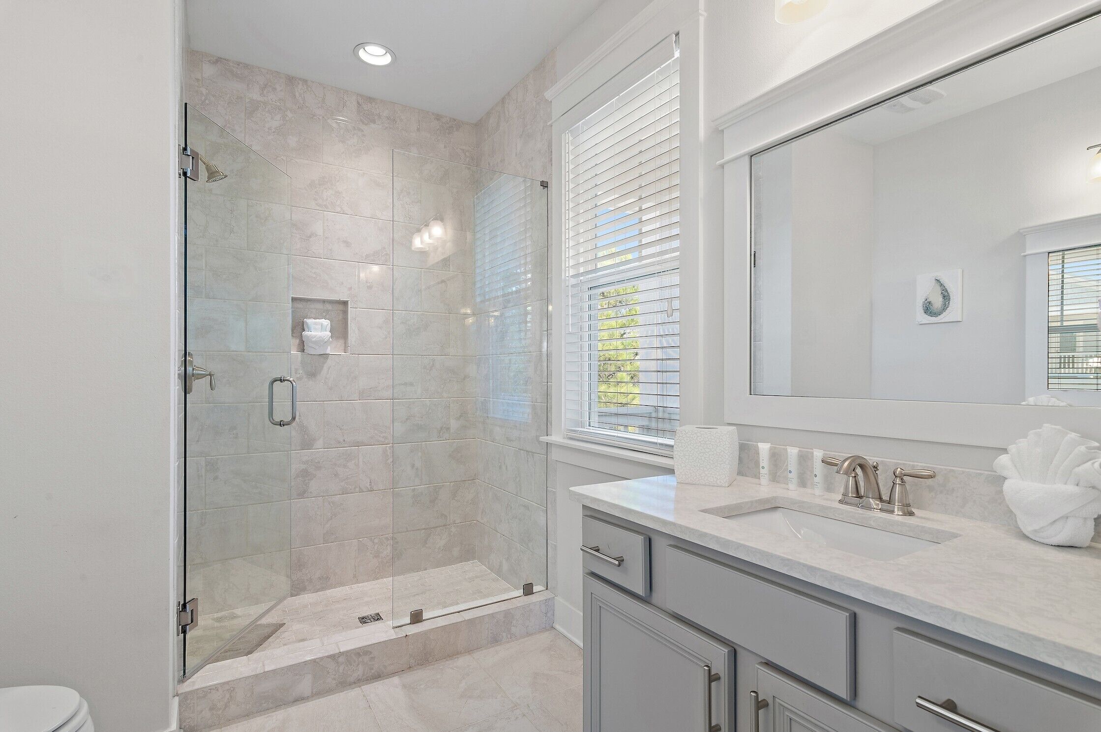 A modern bathroom with a glass-enclosed shower, a large mirror, and a vanity with a sink and cabinet.