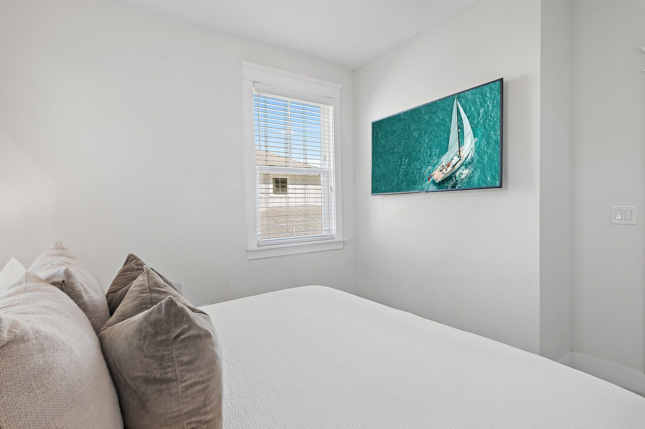 A bedroom with a bed, a window with blinds, and a wall-mounted painting of a sailboat.