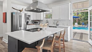 A modern kitchen with a large island, stainless steel appliances, and a view of a pool.