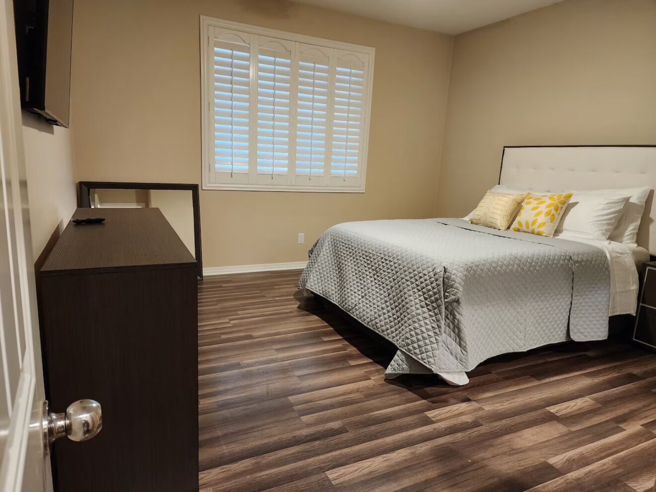 A bedroom with a bed, a dresser, a window with blinds, and a door.