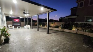 An outdoor patio area with a covered seating area, a flat-screen TV, and potted plants. - Fabulous 4-bedroom house with AC in Riverside (Riverside)