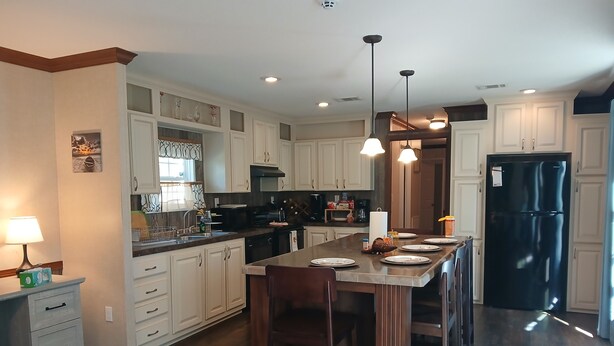 A spacious kitchen with a central island, white cabinetry, and a black refrigerator. - Lots of open and private space for the family and pets (Fanning Springs)