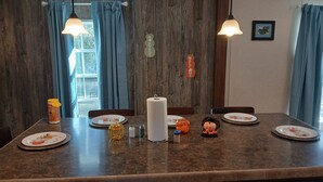 A dining area with a wooden wall, blue curtains, a welcome sign, and a table set with plates, a vase, and a pumpkin decoration. - Lots of open and private space for the family and pets (Fanning Springs)