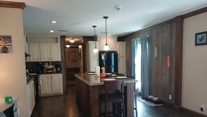 A modern kitchen with white cabinets, a central island with bar stools, and a dining area with a wooden table and chairs. - Lots of open and private space for the family and pets (Fanning Springs)