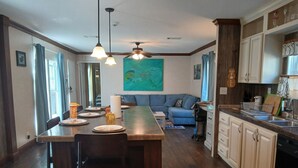 A modern kitchen with wooden cabinets, a dining area with a long table, and a blue sofa in the living room. - Lots of open and private space for the family and pets (Fanning Springs)