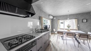 A modern kitchen with a gas stove, sink, and a dining area with a table and chairs. - SASAMEYUKI (Furano)