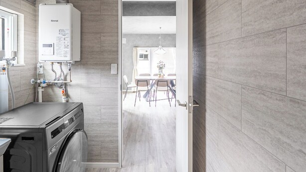 A modern kitchen with a built-in washer and dryer, a dining area with chairs and a table, and a view into the adjacent room. - SASAMEYUKI (Furano)