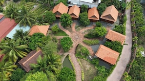 An aerial view of a resort with multiple bungalow-style buildings, surrounded by lush greenery and palm trees. - Rooster Mekong Resort (Cho Lach)
