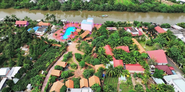 An aerial view of a resort with a swimming pool, multiple bungalow-style buildings, and a river. - Rooster Mekong Resort (Cho Lach)