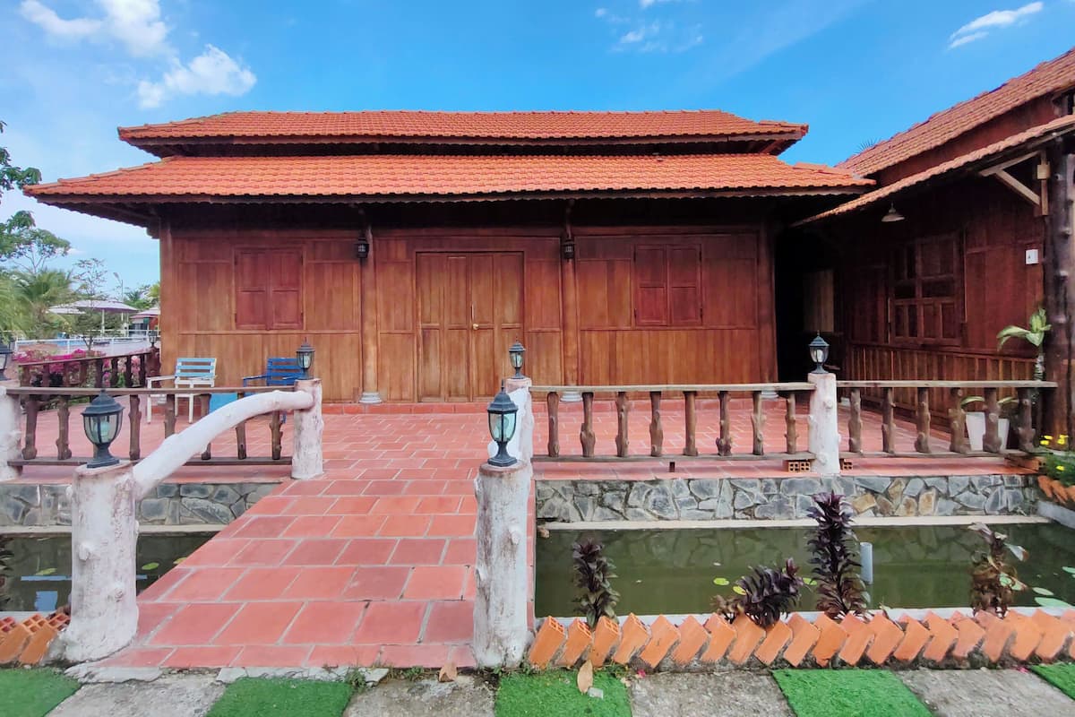 A traditional wooden building with a tiled roof, a stone pathway leading to a wooden gate, and a small pond with plants.