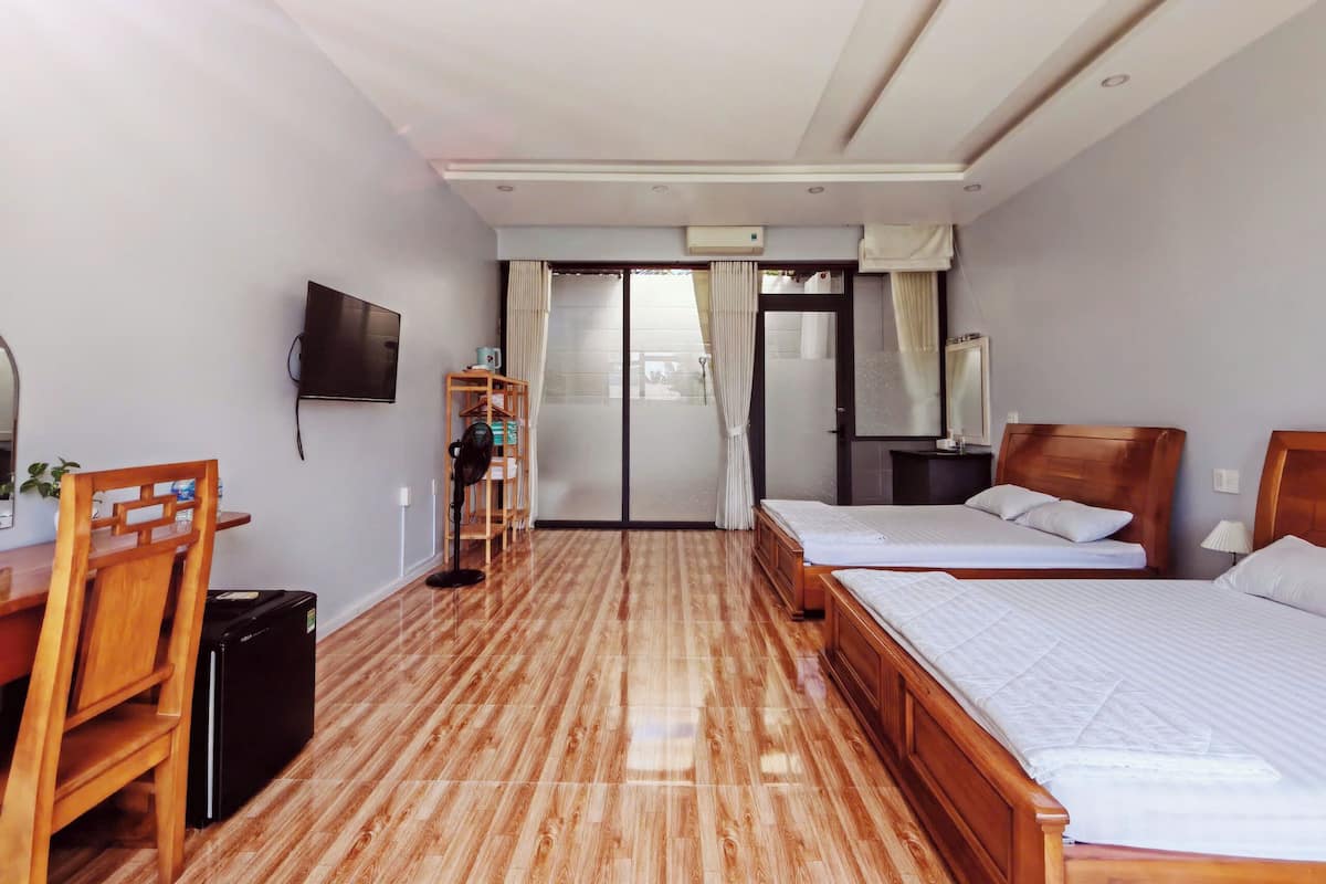 A hotel room with two beds, a desk with a chair, a TV, and a wardrobe.