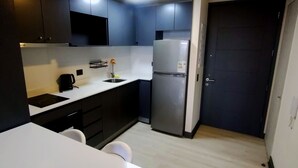 A compact kitchen with dark cabinets, a white countertop, a stainless steel refrigerator, and a black coffee maker. - Your ideal place in the ideal sector of Santiago. 3rd floor (Ñuñoa)