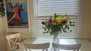 A dining area with a glass-top table, white chairs, and a vase of flowers.