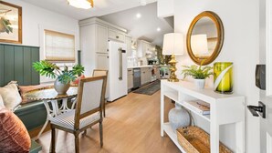 Une cuisine moderne avec des meubles blancs, un îlot central et un coin repas agrémenté d’une chaise à rayures et d’une plante.
