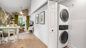 Une buanderie équipée d’un lave-linge et d’un sèche-linge à chargement frontal, un coin repas avec une table et des chaises, et un salon avec un canapé et une table basse.