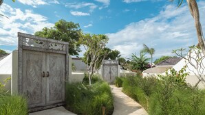 A pathway leading to a gated entrance with a decorative metal gate, surrounded by lush greenery and palm trees. - Naluna Glamping Lembongan (Lembongan Island)