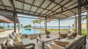 A covered outdoor seating area with a pool, wooden furniture, and a view of the ocean. - Naluna Glamping Lembongan (Lembongan Island)
