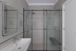 A modern bathroom with a glass-enclosed shower, a white sink, and a mirror. - Three Bedroom Duplex at Eastown Sodic, New Cairo (New Cairo)