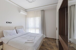A modern hotel room with a large bed, a wooden wardrobe, and a large window with curtains. - Three Bedroom Duplex at Eastown Sodic, New Cairo (New Cairo)
