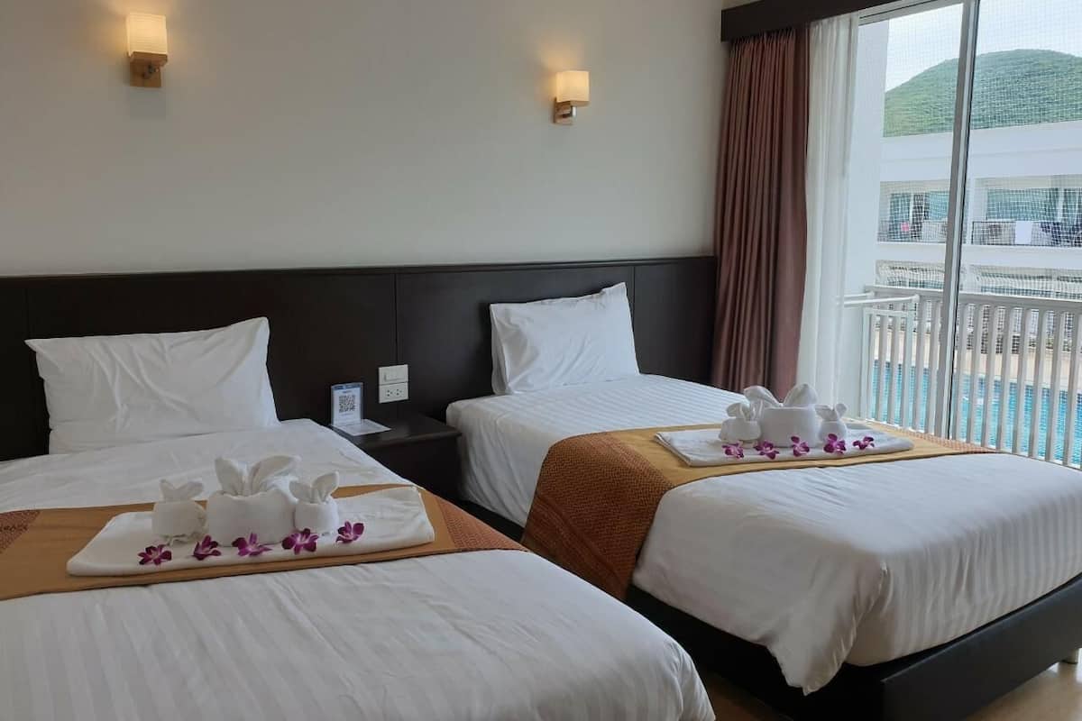 Une chambre d’hôtel avec deux lits, chacun équipé de draps et de serviettes blancs, d’une tête de lit en bois et donnant sur une piscine par une grande fenêtre.