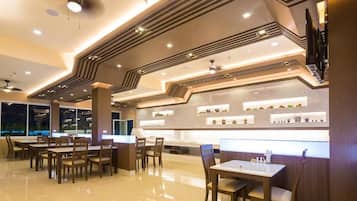A modern restaurant with a sleek design, featuring a long counter, multiple seating areas, and a polished floor.