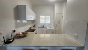 A modern kitchen with white cabinets, a granite countertop, a window with blinds, and a door with a notice.