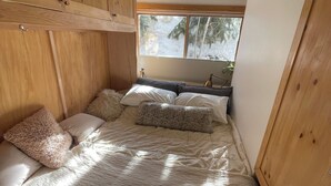 Un dormitorio con una cama, un armario de madera y una ventana con vistas a árboles.