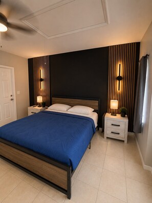 A bedroom with a bed, two bedside tables, a ceiling fan, and a dark wall with vertical lines. - 4BR 2BA Pool Hot Tub BBQ Mini Golf Sleep 12 (Port Charlotte)
