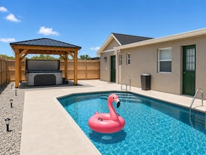 A swimming pool with a flamingo float, a covered patio, and a building with a door and windows. - 4BR 2BA Pool Hot Tub BBQ Mini Golf Sleep 12 (Port Charlotte)