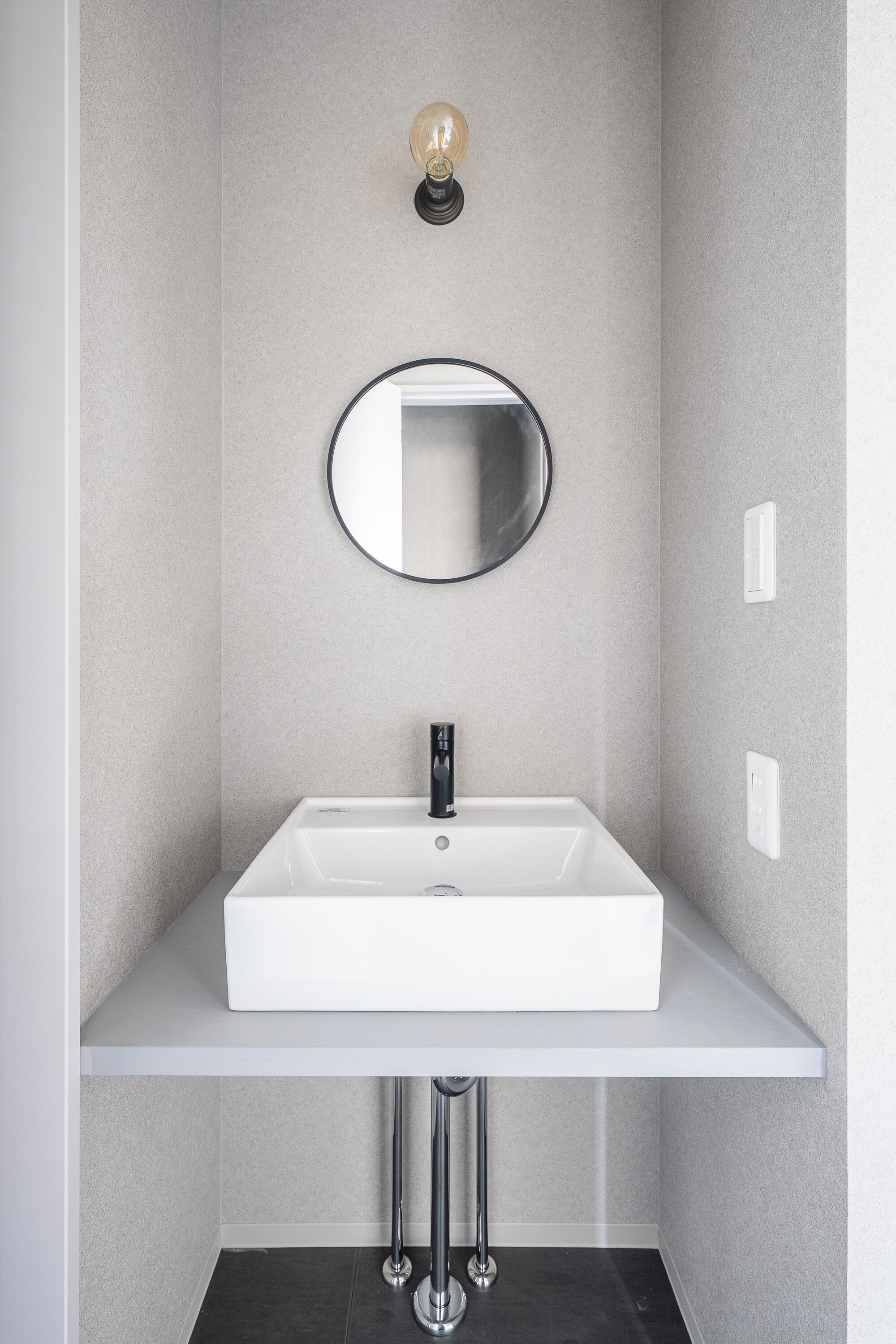 Ein modernes Badezimmer mit einem weißen Waschbecken, einem runden Spiegel und einer Leuchte darüber.