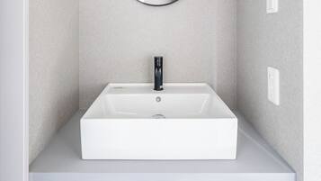 Ein modernes Badezimmer mit einem weißen Waschbecken, einem runden Spiegel und einer Leuchte darüber.