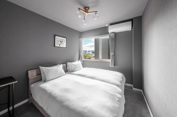 A modern bedroom with a large bed, a bedside table, a window with curtains, and a ceiling light fixture.